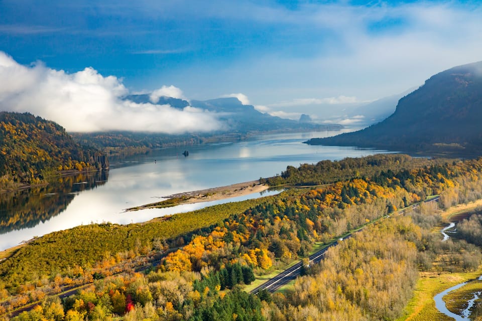A river winding through a forested valley with autumn foliage, a bridge crossing the river, and a road running parallel to the river.