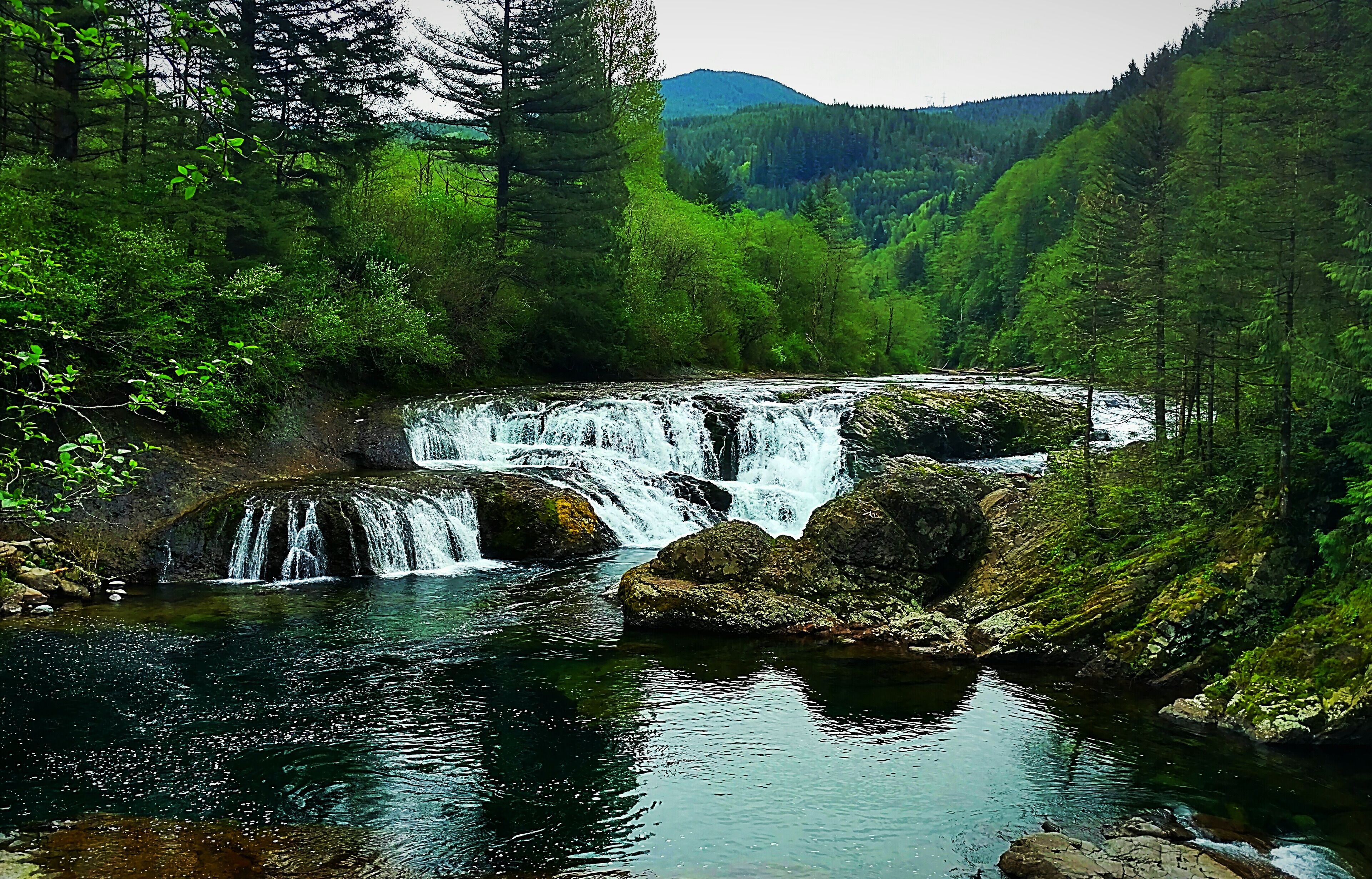 A waterfall in a forested valley with a mountain in the background.