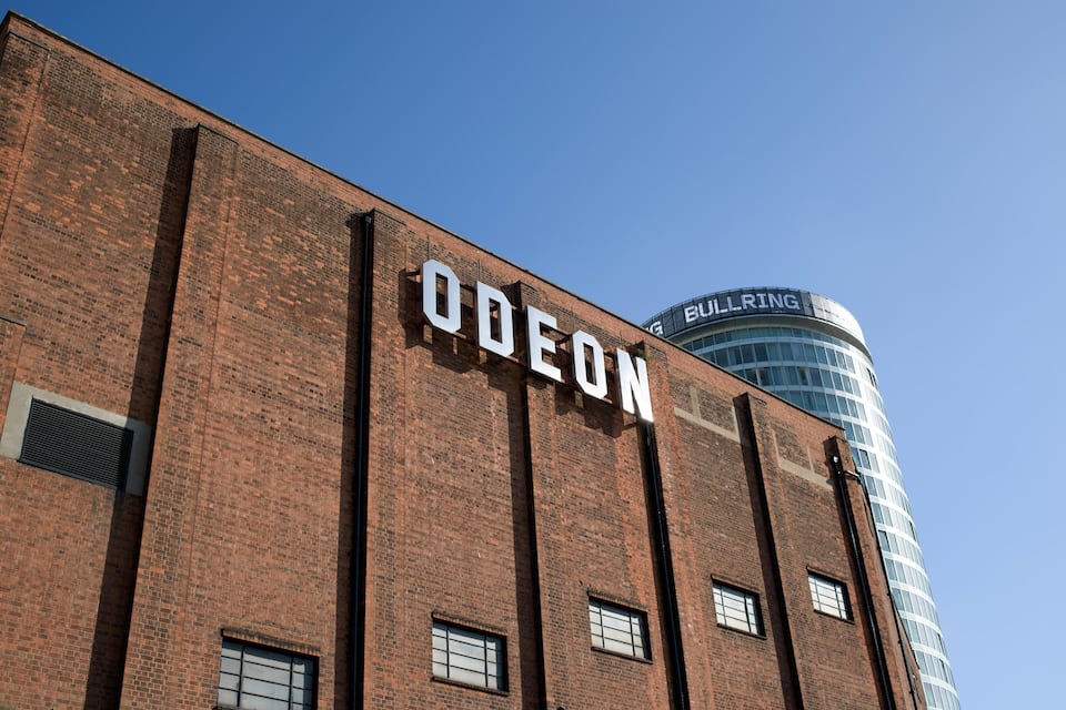 Edifici de maó amb la paraula "ODEON" a la façana i un edifici modern de vidre al fons anomenat "BULLRING".