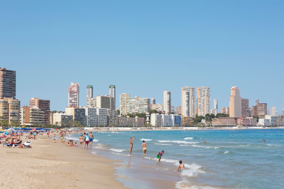 A beach with people swimming and sunbathing, and a city skyline in the background.