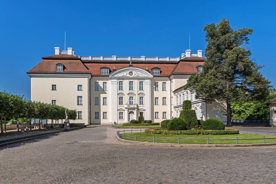 Um edifício grande e histórico, com fachada simétrica, entrada central e jardim bem cuidado.