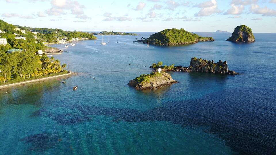 A coastal landscape with clear blue waters, several small islands, and a distant shoreline with buildings.