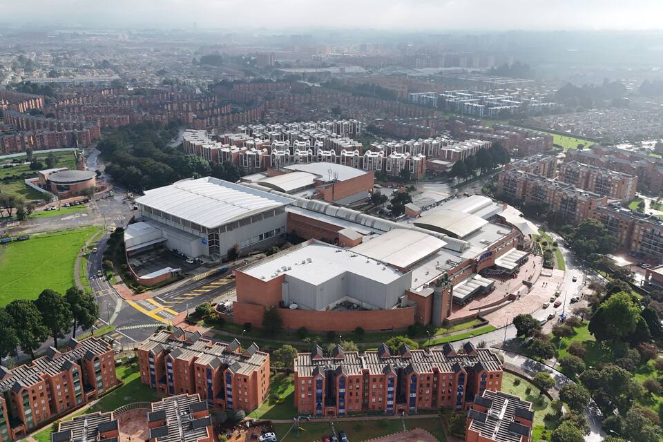 Une vue aérienne d’un vaste complexe industriel composé de plusieurs bâtiments, entouré de zones résidentielles et d’espaces verts.