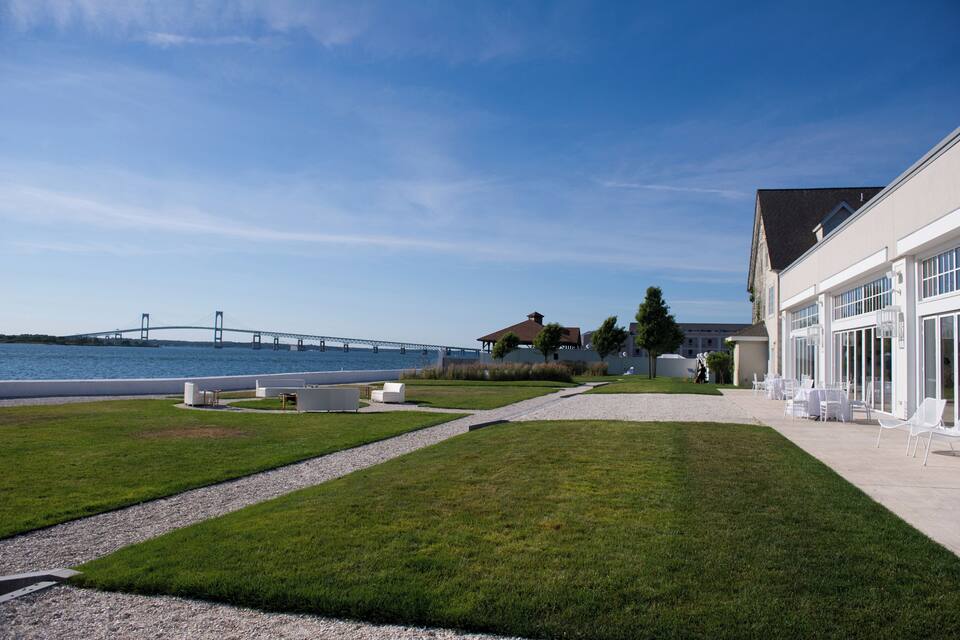 A waterfront property with a bridge in the background, a lawn, and a building with outdoor seating.