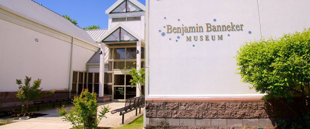 The exterior of the Benjamin Banneker Museum with a clear sky, a white building, and a small garden area with benches.