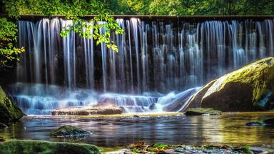 A waterfall cascading over rocks into a calm pool surrounded by lush greenery.