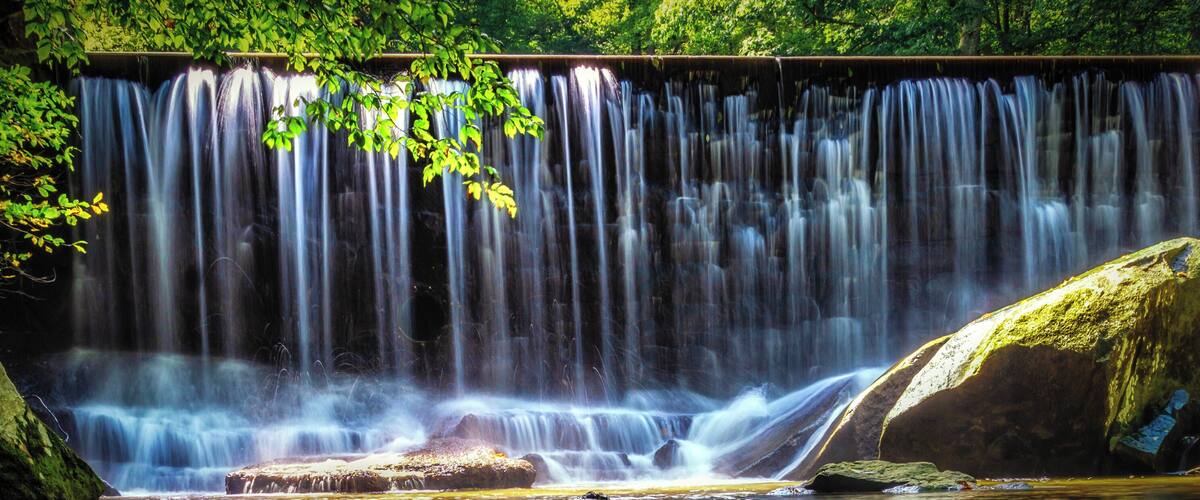 A waterfall cascading over rocks into a calm pool surrounded by lush greenery.