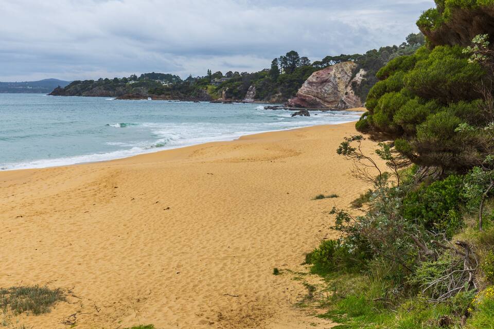 A sandy beach with gentle waves, a rocky cliff, and lush greenery.