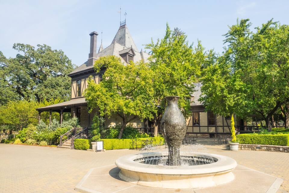 A historic building with a turret and a fountain in a landscaped garden.