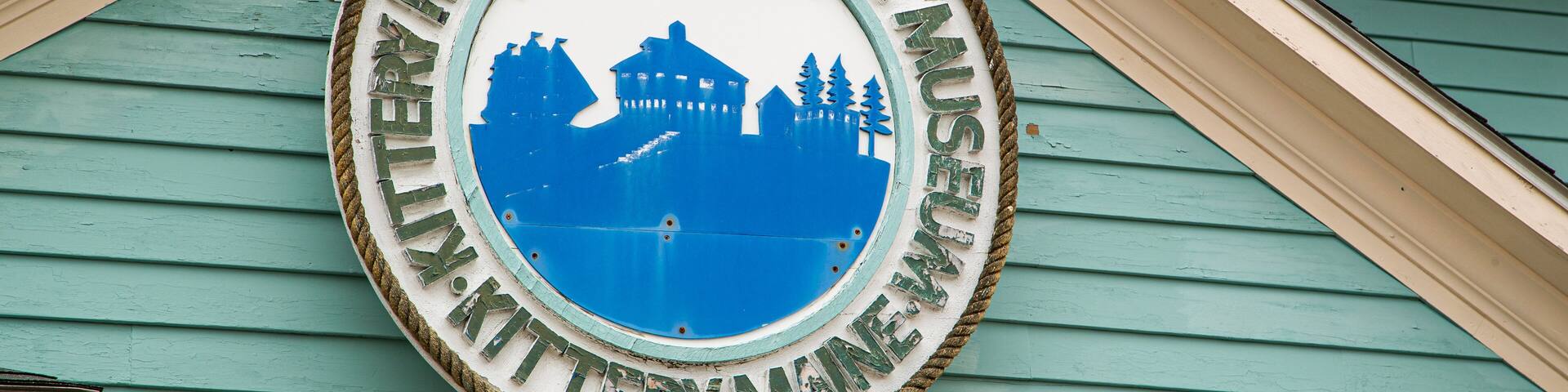 A circular sign with a blue silhouette of a building and trees, surrounded by a rope border, on a green building facade.
