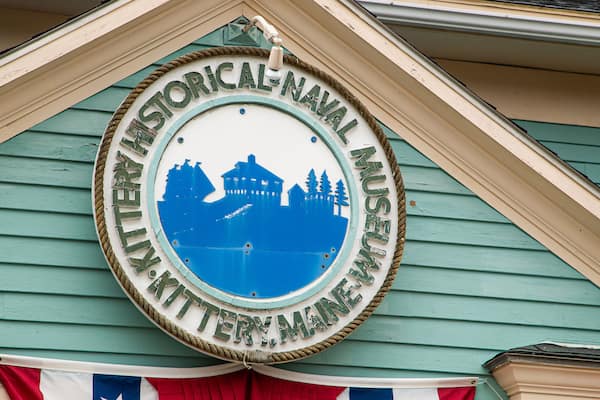 A circular sign with a blue silhouette of a building and trees, surrounded by a rope border, on a green building facade.
