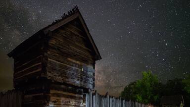Une cabane en bois rustique, sous un ciel étoilé.
