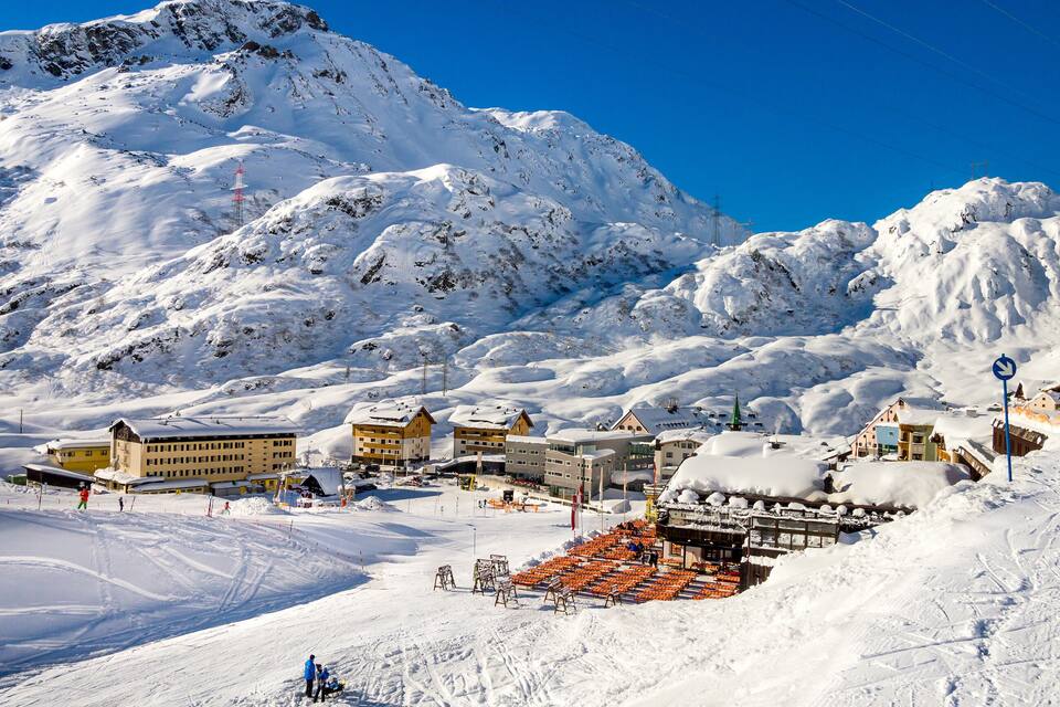 Een skigebied bedekt met sneeuw, met gebouwen, skiliften en een berg op de achtergrond.