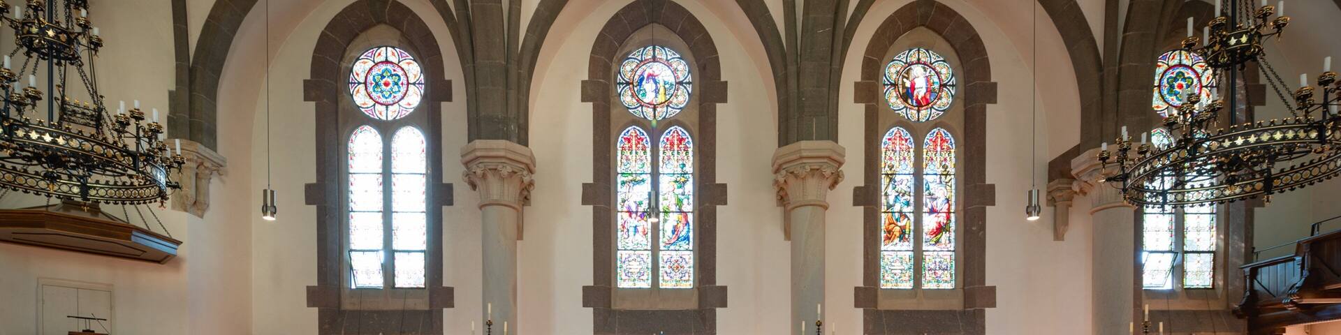 A church interior with wooden pews, stained glass windows, and a chandelier.