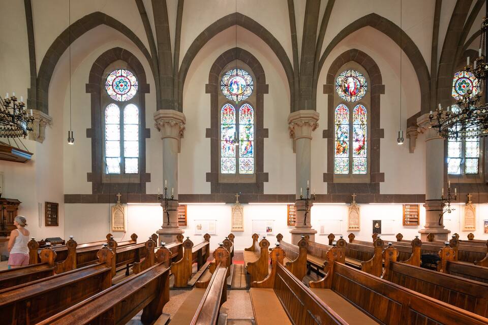 A church interior with wooden pews, stained glass windows, and a chandelier.