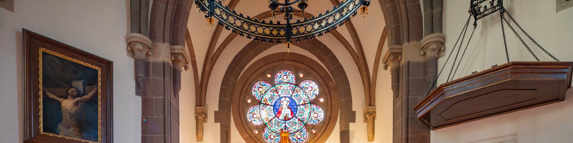 A church interior with a large stained glass window, a crucifix, and a wooden pulpit.