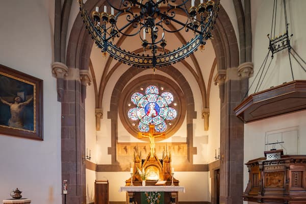 L’intérieur d’une église, avec une grande fenêtre à vitraux, un crucifix et une chaire en bois.