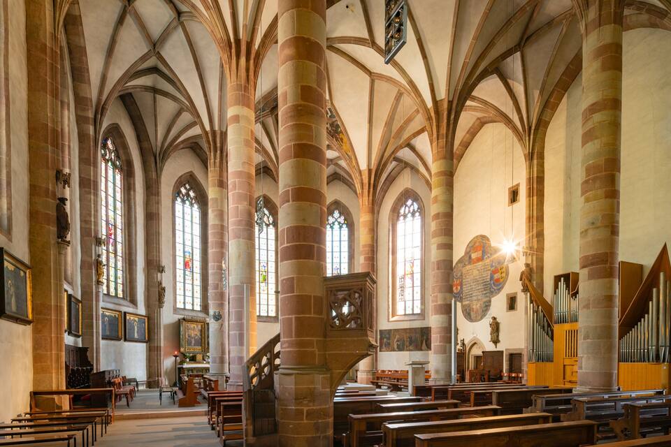 A church interior with high vaulted ceilings, stained glass windows, and a pipe organ.