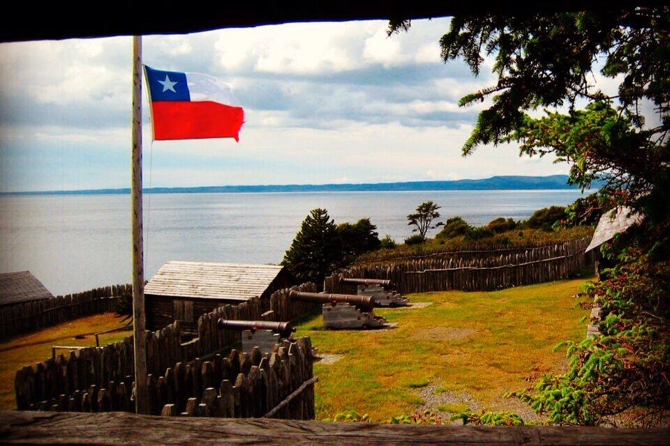 Una bandera en un pal, una tanca de fusta i un cos d'aigua al fons.