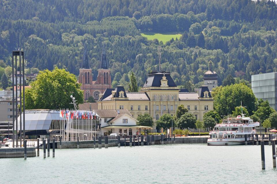 A riverside town with historic buildings, a church, and a boat docked at the pier.