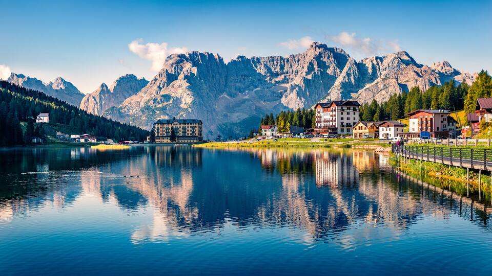 A lake with reflections of buildings and mountains in the background.