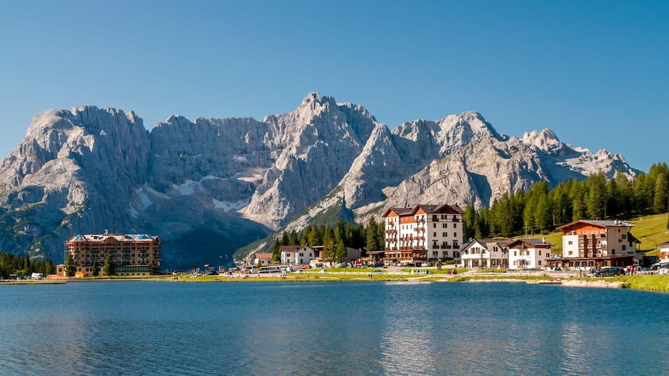 A lake with buildings and mountains in the background.