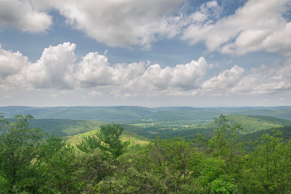 Paisagem montanhosa com colinas ondulantes e densas florestas verdes sob um céu parcialmente nublado.