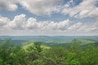 Eine gebirgige Landschaft mit sanften Hügeln und dichten, grünen Wäldern unter einem teilweise bewölkten Himmel.