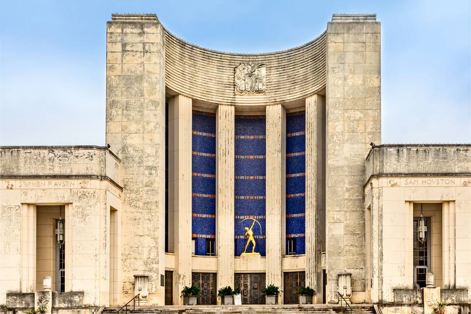 A large building with a curved roof and a statue of a figure holding a spear.