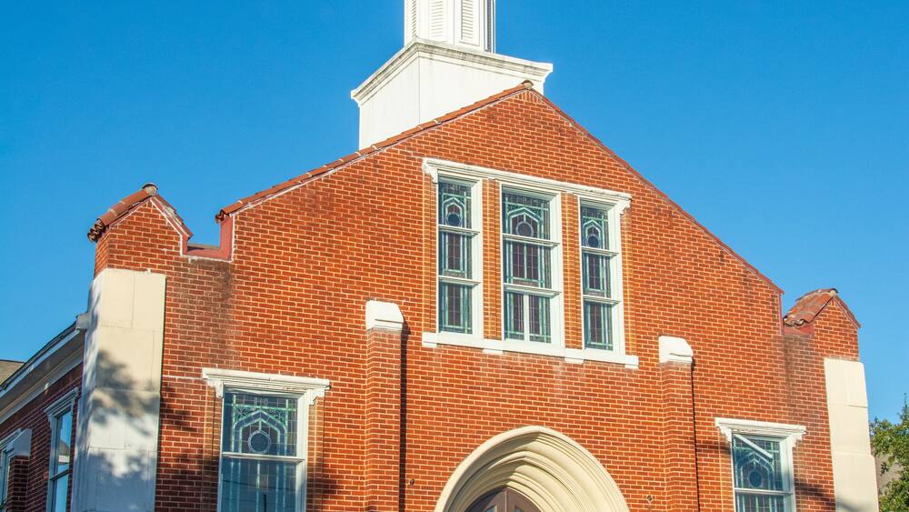 Une église en briques rouges, dotée d’un clocher blanc et d’une entrée en arc de cercle.