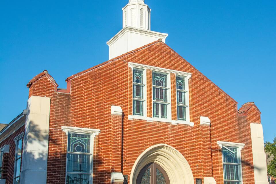 A red brick church with a white steeple and arched entrance.