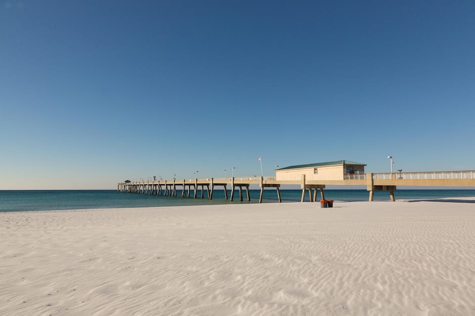 A beach with white sand and a pier extending into the water.