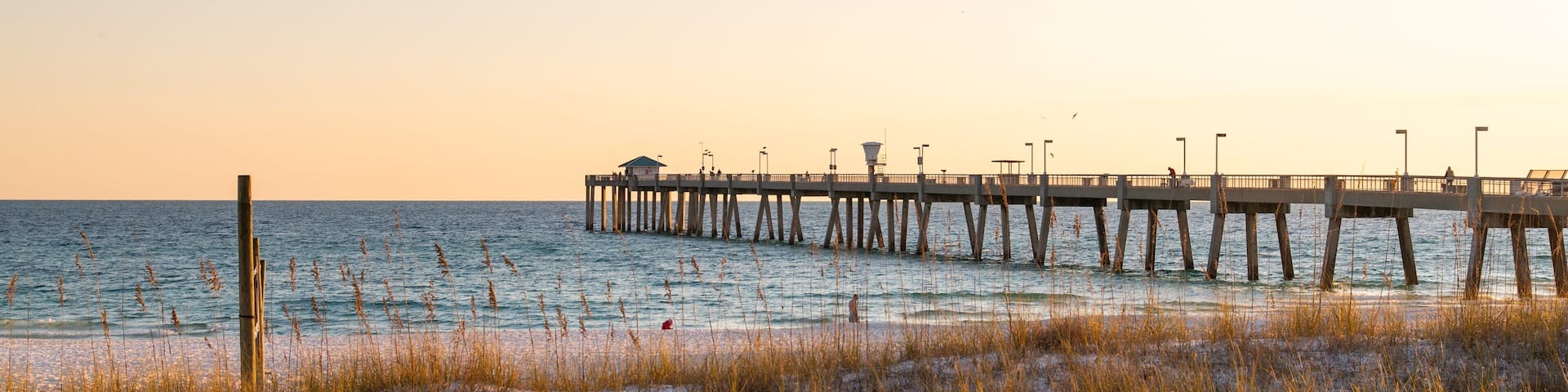A beach with a wooden pier extending into the ocean, featuring a small building and street lamps.