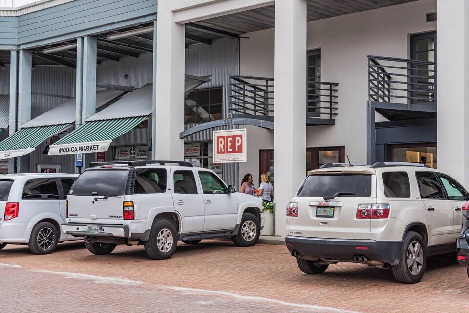 A parking area with white SUVs, a building with a sign reading "REP," and a sign for "MODICA MARKET."