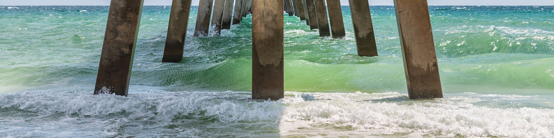 Under Okaloosa fishing pier in Fort Walton Beach, Florida with pillars, green shallow waves in Panhandle, Gulf of Mexico on summer sunny day