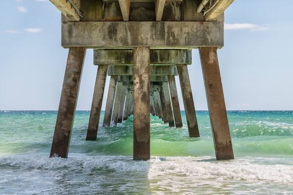 Under Okaloosa fishing pier in Fort Walton Beach, Florida with pillars, green shallow waves in Panhandle, Gulf of Mexico on summer sunny day