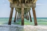 Under Okaloosa fishing pier in Fort Walton Beach, Florida with pillars, green shallow waves in Panhandle, Gulf of Mexico on summer sunny day