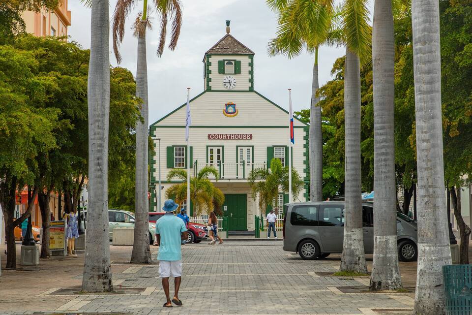 A Courthouse with a clock tower, surrounded by palm trees and parked cars.