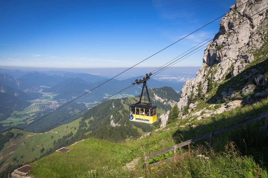 Eine Seilbahn im Wendelstein-Tal, die über eine gebirgige Landschaft mit blauem Himmel schwebt.