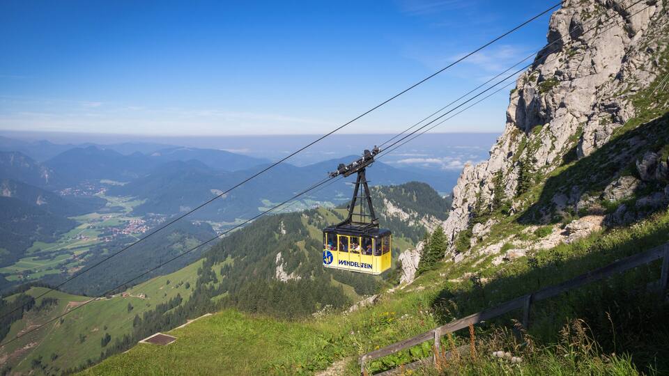 A cable car in Wendelstein Valley, suspended over a mountainous landscape with a clear sky.