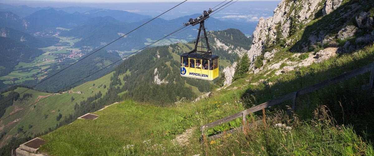 A cable car in Wendelstein Valley, suspended over a mountainous landscape with a clear sky.