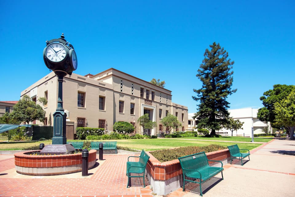 A clock tower, green benches, and a building with a brick facade.