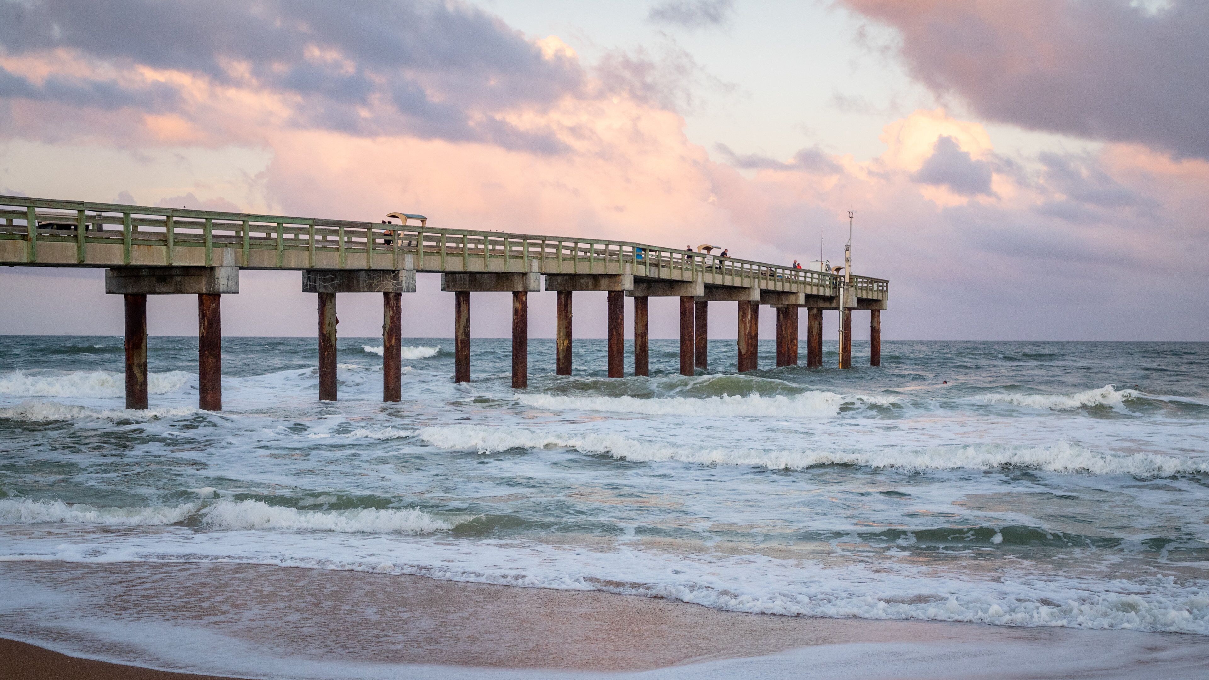 A pier extending into the ocean with waves crashing against it.