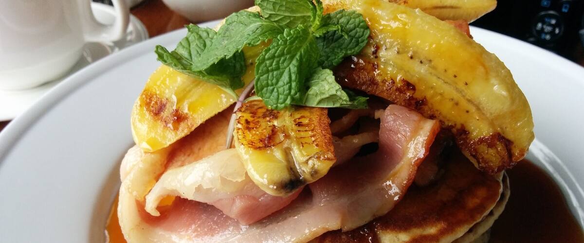 A stack of pancakes with bacon, pineapple, and a drizzle of syrup on a white plate.