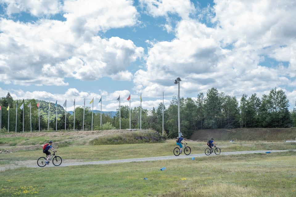 A cyclist on a dirt path with flags and trees in the background.