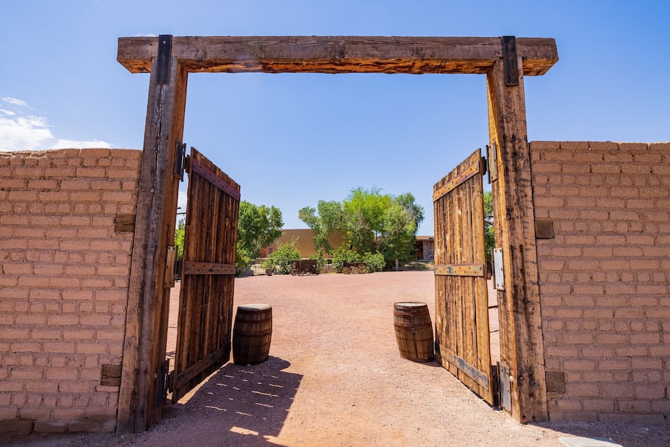 Una rústica puerta de madera da paso a un patio con muros de ladrillo y dos barriles.
