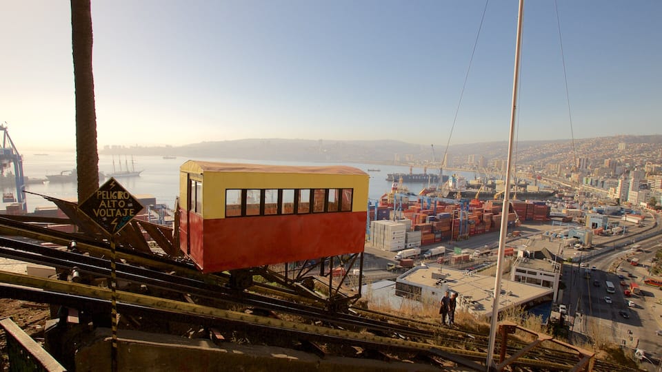 A cable car system with a yellow and red car, a port with shipping containers, and a cityscape in the background.