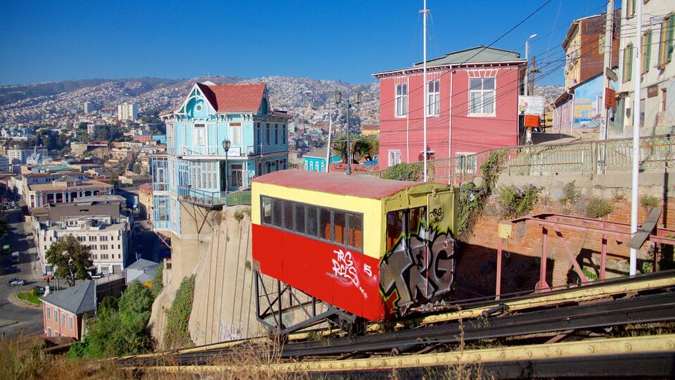 A cable car system with graffiti, a blue house with a red roof, and a cityscape in the background.