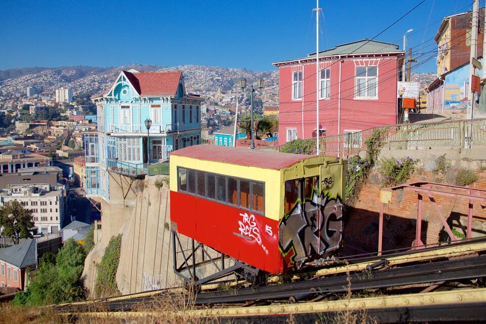 A cable car system with graffiti, a blue house with a red roof, and a cityscape in the background.