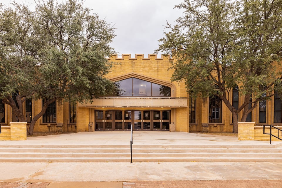 A building with a large arched entrance, surrounded by trees.